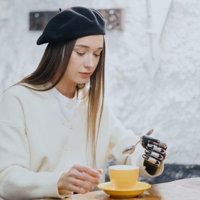 woman with a bionic prosthetic arm is working on a laptop and drinking coffee in a coffee shop